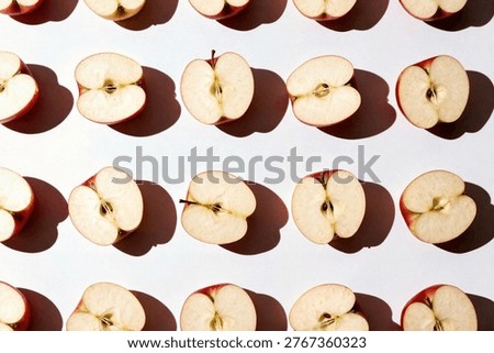 Top view of a pattern created by rows of halved red apples showing the seeds and core on a clean white background.