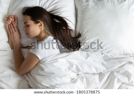 Top view peaceful young woman sleeping on side in cozy bed, calm beautiful female with closed eyes resting on soft pillow under warm duvet, enjoying fresh white bedclothes, relaxing