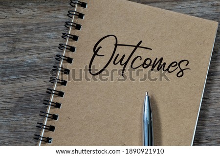 Top view of pen and notebook written with text OUTCOMES over wooden background. 