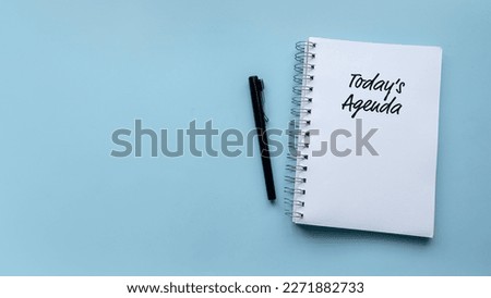 Top view of pen and notebook written with Today's Agenda on blue background with copy space.