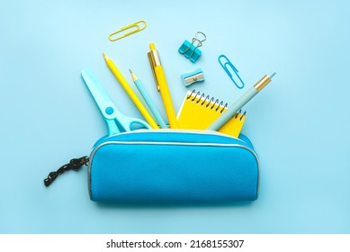 Top view of pencil case with school supplies on blue background. Back to school concept
