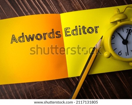 Top view pencil,clock and colored notepaper with text Adwords Editor on wooden background.