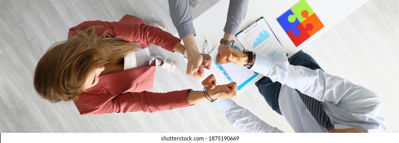 Top view of people celebrate new business contract. Men and woman showing thumbs up standing in office. White desktop with papers. Good deal. Success concept