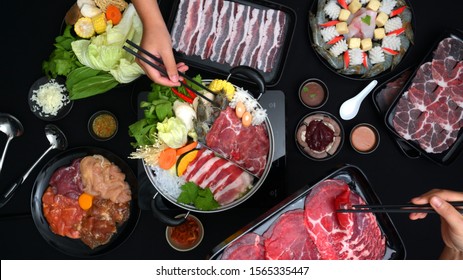 Top View Of People Eating Shabu-Shabu In Hot Pot With Fresh Sliced Meat, Sea Food, And Vegetables With Black Background, Japanese Cuisine