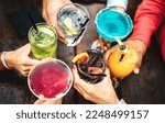 Top view of people hands toasting multicolored fancy drinks - Young friends having fun drinking cocktails at happy hour - Social gathering party concept on vivid filter - Shallow depth of field