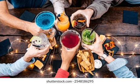 Top view of people toasting glasses of fancy multicolored drinks at restaurant bar - Young friends having fun drinking cocktails at happy hour at pub - Social gathering home party life style concept