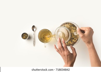 top view of person pouring fresh organic herbal tea from kettle into glass on white