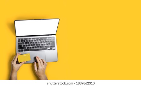 Top view person shopping online with their laptop and using a yellow credit card to pay for products, copy space for advertising images, Isolated on yellow background and clipping path.