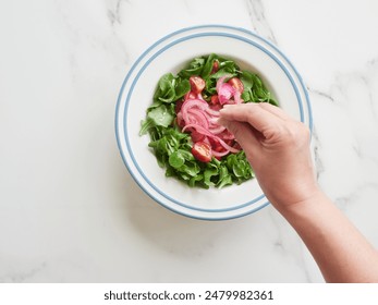 Top view of a person's hand dressing a plate of colorful salad with a pinch of salt. - Powered by Shutterstock