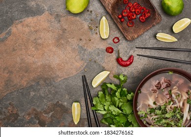 Top View Of Pho In Bowl Near Chopsticks, Lime, Chili And Coriander On Stone Background