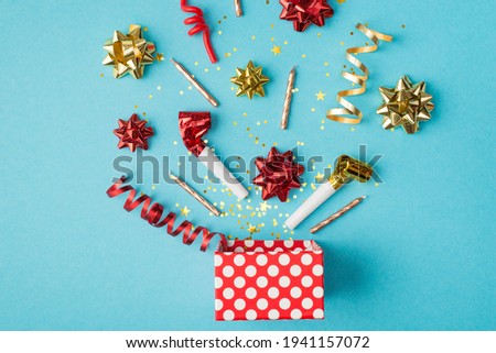 Top view photo of birthday composition blast of tinsel sparkles serpentine red yellow golden ribbon stars pipes and candles on isolated blue background with copyspace