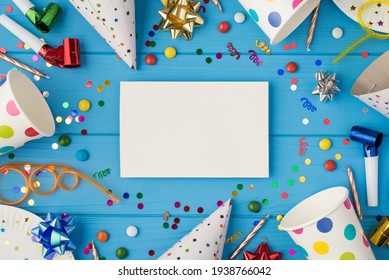 Top View Photo Of Birthday Party Composition White Card With Copyspace In The Middle Spiral Tubes Ribbon Stars Candles Pipes Hats Confetti Paper Cups And Plates Isolated Blue Wooden Table Background