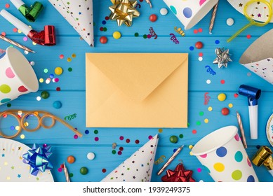 Top View Photo Of Birthday Party Composition Closed Craft Paper Envelope In The Middle Spiral Tubes Ribbon Stars Candles Pipes Hats Confetti Paper Cups And Plates Isolated Blue Wooden Table Background