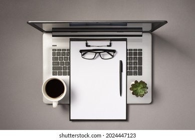 Top view photo of black clipboard with white sheet of paper glasses pen cup of drink and flowerpot on open laptop on isolated grey background with empty space - Powered by Shutterstock