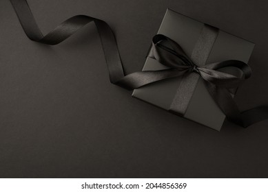 Top view photo of black gift box with black ribbon bow on isolated black background with empty space