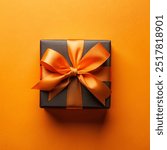 Top view photo of black giftbox with orange satin ribbon bow on isolated orange background with empty copy-space