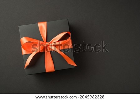 Top view photo of black giftbox with orange satin ribbon bow on isolated black background with copyspace