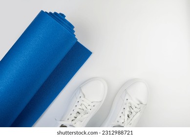 Top view photo of a blue fitness mat and white sneakers on a white background.The concept of fitness, yoga, sports. - Powered by Shutterstock