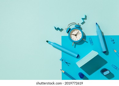 Top view photo of blue school accessories stationery markers pencils sticky note paper clips pushpins and ringing alarm clock on isolated pastel blue background with copyspace
