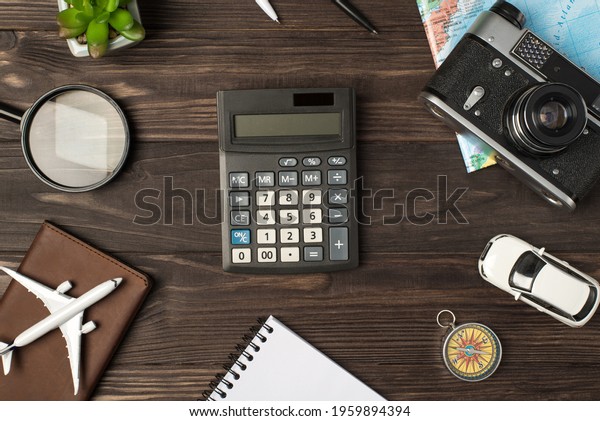 Top view photo of calculator in\
the center plane and car models camera map magnifier compass\
notebook passport cover and plant on isolated wooden table\
background