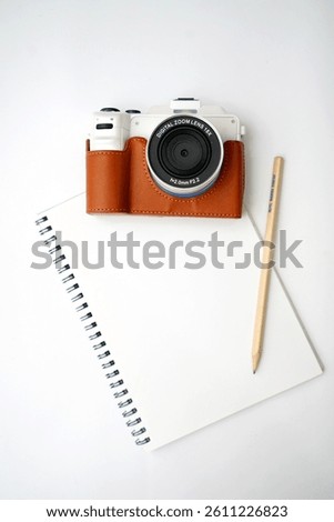 top view of photo camera, notepad with pencil on white                               