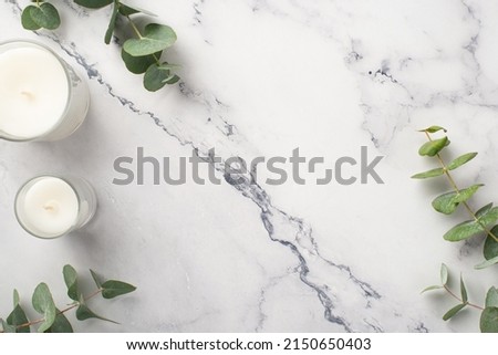 Top view photo of candles with glass holders and eucalyptus on white marble background with copyspace