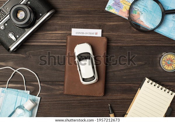 Top view\
photo of car model on leather passport cover with covid test camera\
map magnifier compass notebook pen medical masks and sanitizer on\
isolated wooden table\
background