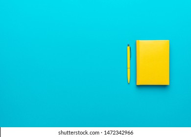 Top view photo of closed yellow notebook and ball-point pen over turquoise blue background with copy space. Minimalist flat lay image of closed diary and yellow pen as back to school background.