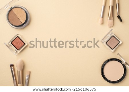 Top view photo of contouring palette compact powder eyeshadow containers and makeup brushes on pastel beige background with copyspace
