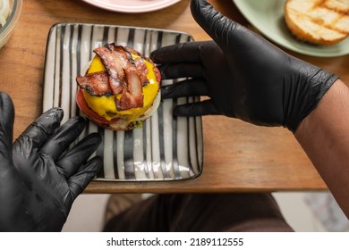 Top View Photo Of A Cook With Latex Gloves Plating A Burger In A Ceramic Plate In A Kitchen