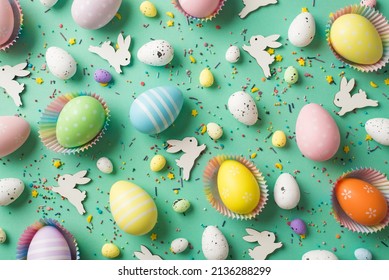 Top view photo of easter decorations multicolored easter eggs in paper baking molds confectionery topping and easter bunnies on isolated pastel green background