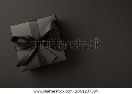 Top view photo of giftbox in black packaging with black satin ribbon bow and tag on isolated black background with copyspace