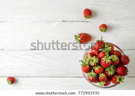 Top view photo of a glass plate with ripe red strawberries on a white wooden table. Four strawberries scattered on a table. Macro photo of ripe strawberries. Place for text.
