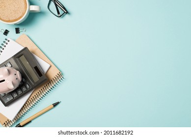 Top view photo of glasses cup of frothy coffee binder clips pen planner and piggy bank on calculator on isolated pastel blue background with copyspace - Shutterstock ID 2011682192