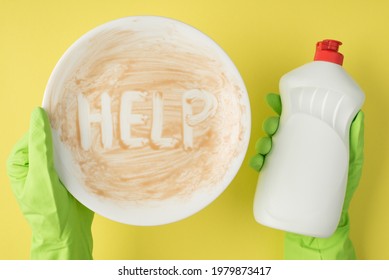 Top View Photo Of Hands In Green Rubber Gloves Holding Dirty Dish With Inscription Help And White Bottle Foam Detergent Without Label On Isolated Yellow Background With Blank Space