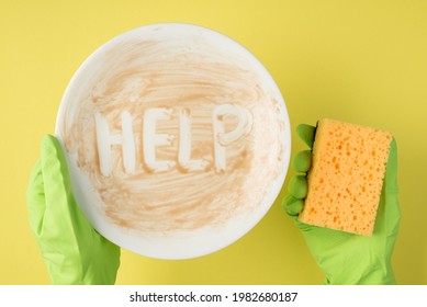 Top View Photo Of Hands In Green Rubber Gloves Holding Dirty Dish With Inscription Help And Yellow Sponge On Isolated Yellow Background