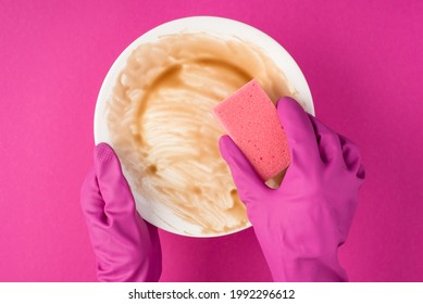 Top View Photo Of Hands In Pink Rubber Gloves Holding Dirty Dish And Using Pink Scouring Pad On Isolated Pink Background
