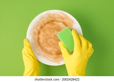 Top View Photo Of Hands In Yellow Rubber Gloves Holding Dirty Dish And Green Sponge On Isolated Green Background