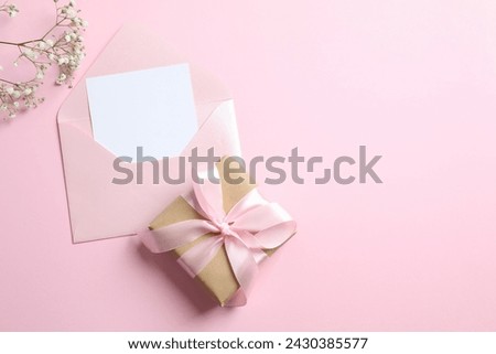 Top view photo of open envelope with paper card, giftbox and white gypsophila flowers on pastel pink background with empty space