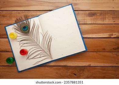 Top view photo of opened Diary, fabric colors, and a Peacock Feather over it. On a wooden background. Flat lay image of blank diary. 庫存照片