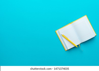 Top view photo of opened notebook and yellow pen over it on turquoise blue background with copy space. Minimalist flat lay image of blank diary and ball-point pen