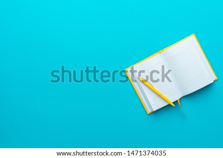 Top view photo of opened notebook and yellow pen over it on turquoise blue background with copy space. Minimalist flat lay image of blank diary and ball-point pen