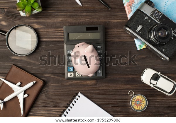 Top view photo\
of piggy bank on calculator in the center plane and car models\
camera map magnifier compass notebook passport cover and plant on\
isolated wooden table\
background