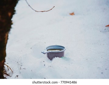 Top view photo of a pink plastic mug filled with tea, standing on a rock partly covered with snow. Drinking hot beverage outdoors on a winter day. Thermos cap with tea.