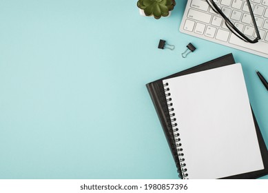 Top view photo of planners pen binders plant and glasses on keyboard on isolated pastel blue background with copyspace