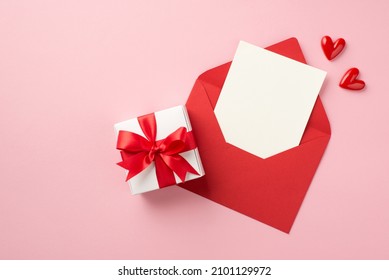 Top view photo of saint valentine's day decorations small hearts white giftbox with red bow open red envelope with paper card on isolated pastel pink background with empty space