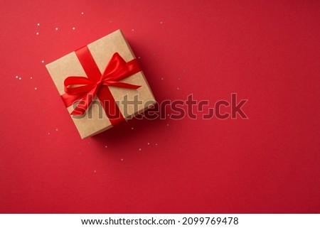 Top view photo of saint valentine's day decorations glowing sequins and craft paper giftbox with red ribbon bow on isolated red background with copyspace