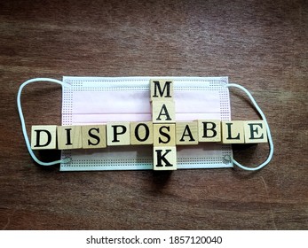 Top View Photo Of Square Wood Blocks Crossword With The Words DISPOSABLE MASK On A Disposable Face Mask, Isolated On A Wooden Ground Sheet.