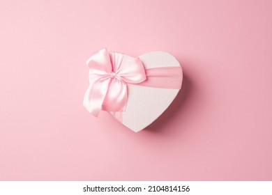 Top view photo of valentine's day decorations heart shaped giftbox with pink ribbon bow on isolated pastel pink background with copyspace