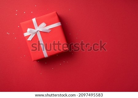 Top view photo of valentine's day decorations glowing sequins and red giftbox with white ribbon bow on isolated red background with copyspace